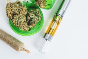image of various marijuana products including a rolled joint, a vape pen and fresh flower on a white background